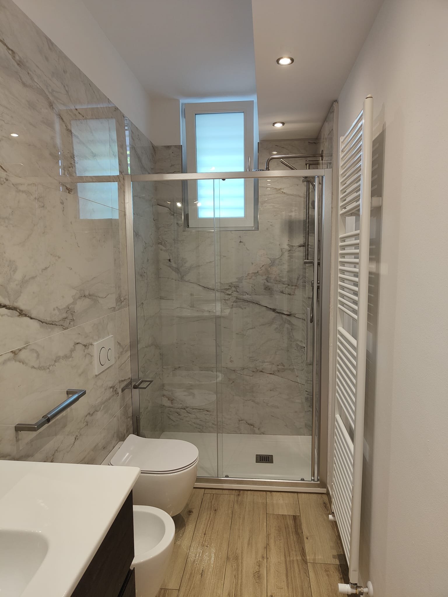 Bagno ristrutturato con rivestimento effetto marmo e doccia in vetro